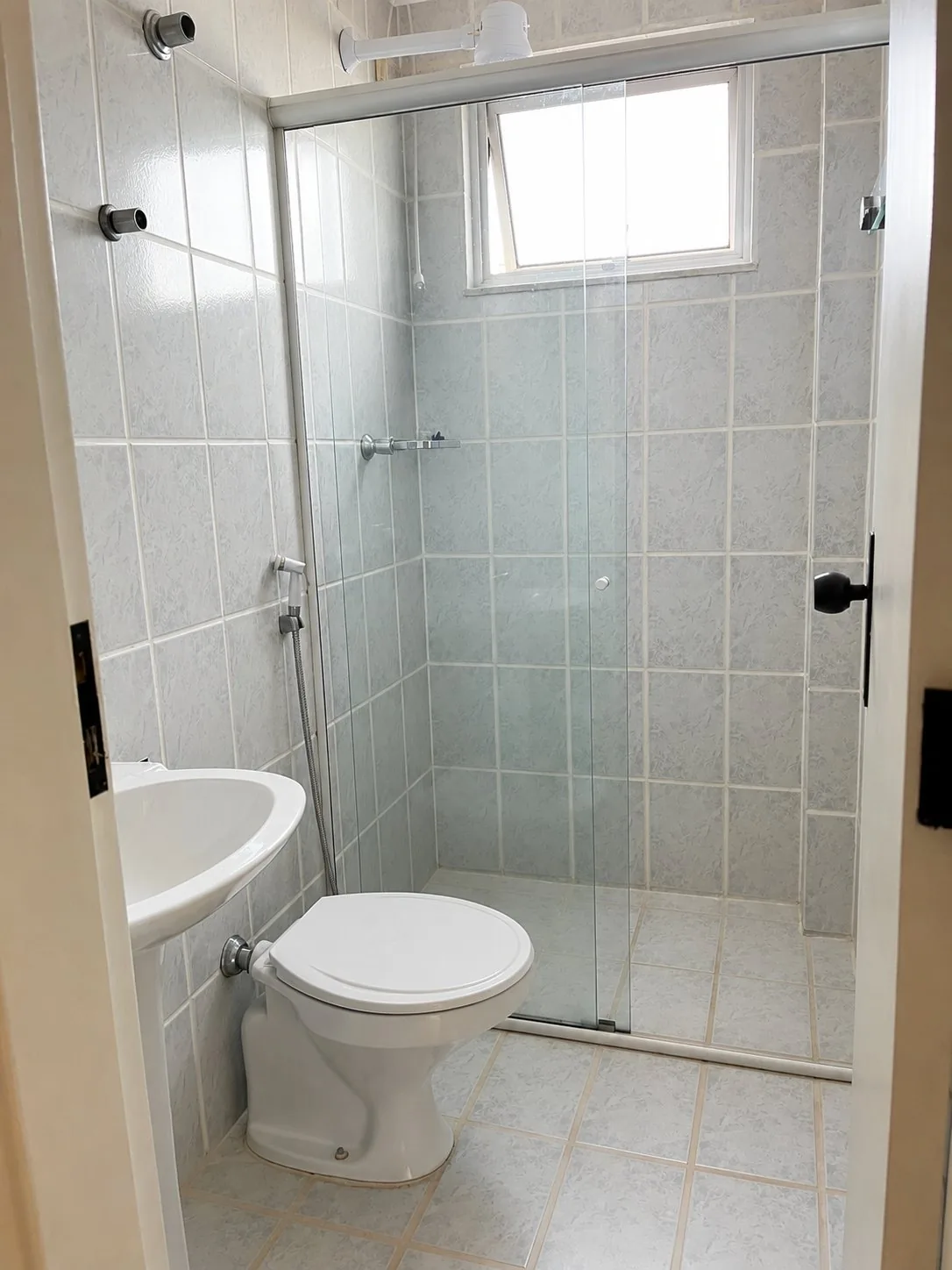 Banheiro da suíte com box em blindex e revestimento claro, no apartamento do Santa Rosa.